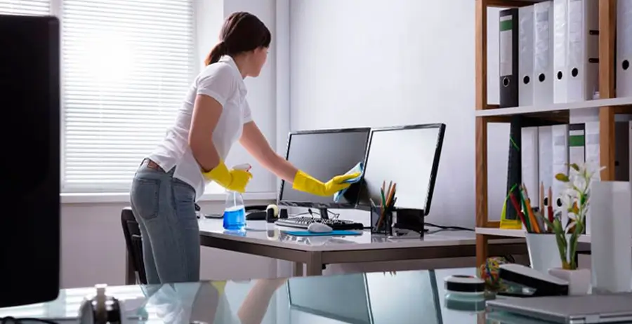 Janitor cleaning computer monitors on office desk