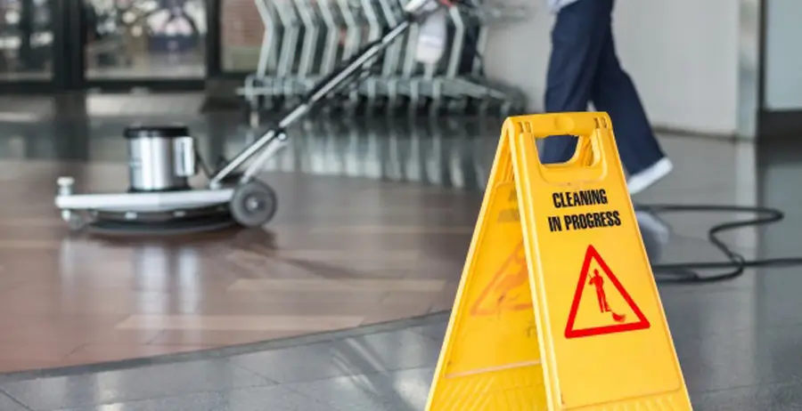 person using floor waxing machine behind sign titled "cleaning in progress"