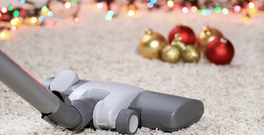 Vacuum cleaner on carpet with blurry holiday ornaments in background.