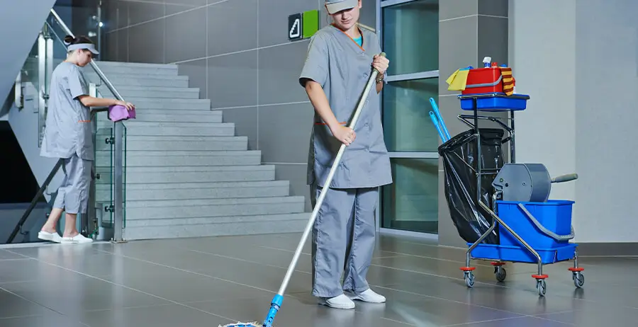 Two janitors cleaning floor and wiping down surfaces in office building