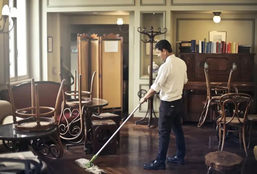 Dry mop being used on the floor of a restaurant or cafe with chairs on the tables.