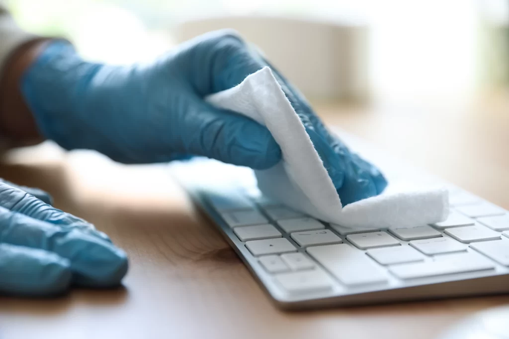 Gloved hands wiping a keyboard with a cloth.